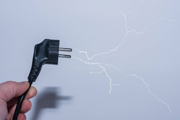 βύσμα στο ένα χέρι εκτός από την ηλεκτρική ενέργεια και μια διακλαδισμένη αστραπή με γκρι backgroun - Φωτογραφία, εικόνα