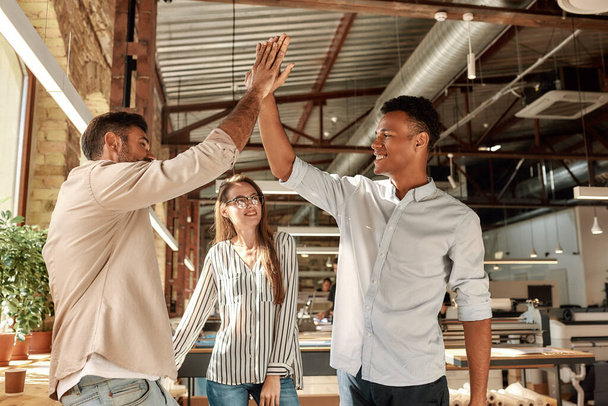 Twee vrolijke mannen geven high-five terwijl staan met collega 's in het moderne kantoor - Foto, afbeelding