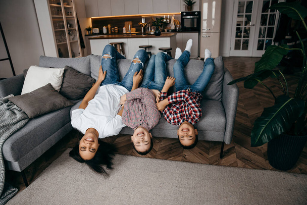 Felice famiglia mamma e due figli scherzare e sdraiarsi a testa in giù sul divano - Foto, immagini