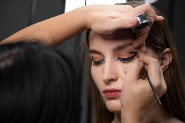 Make-up artist drawing eye line on beautiful model face finishing her make up for professional photoshoot or commercial. Portrait of a brunette model girl in make up studio applying make up - Фото, зображення