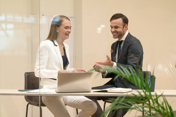 Two laughing project managers discuss updates while having a coffee break. Young business people in the suits with coffee in hands looking down standing behind the glass - Foto, Imagen