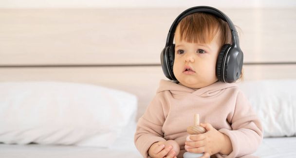 aranyos gyermek lány óvoda hallgat zenét fejhallgató, hang gyerekeknek, boldog gyermekkori koncepció, gyermek egy fehér ágy fülhallgató. Zászlós. másolás helye. - Fotó, kép