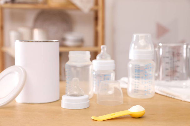 Scoop with powdered infant formula, can and bottles on wooden table indoors. Baby milk - Фото, зображення