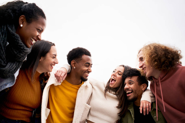 Çok ırklı arkadaş grubu sarılıp eğleniyor. Birbirinden ayrı gülümseyen ve birlikte gülen genç insanlar topluluğun tadını çıkarıyorlar.. - Fotoğraf, Görsel
