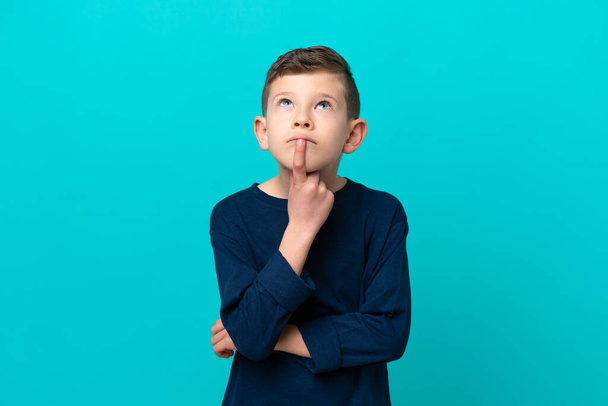 Little kid boy isolated on blue background having doubts while looking up - Photo, image