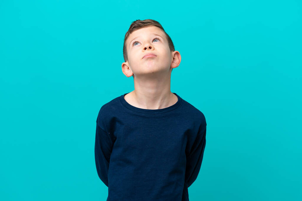 Little kid boy isolated on blue background and looking up - Foto, imagen