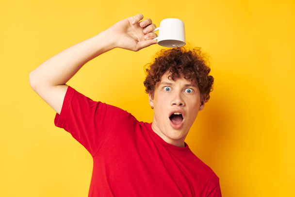 portrait of a young curly man white mug in the hands of a drink yellow background unaltered - Fotoğraf, Görsel