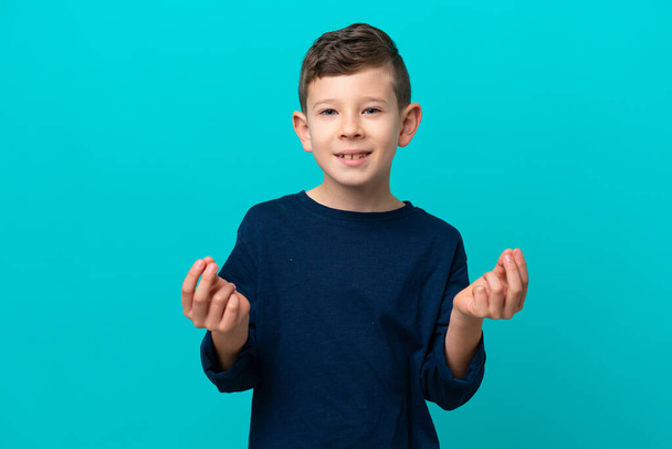 Μικρό αγόρι απομονωμένο σε μπλε φόντο κάνει χειρονομία χρήματα - Φωτογραφία, εικόνα