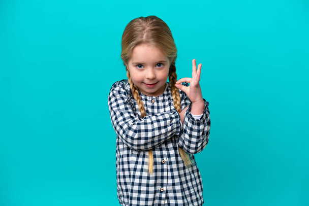 Μικρή καυκάσιος κορίτσι απομονώνονται σε μπλε φόντο δείχνει ok σημάδι με τα δάχτυλα - Φωτογραφία, εικόνα