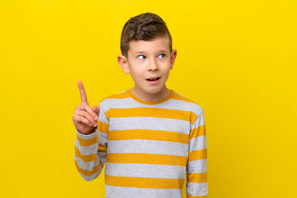 Kleiner kaukasischer Junge isoliert auf gelbem Hintergrund, der die Lösung erkennt, während er den Finger hebt - Foto, Bild