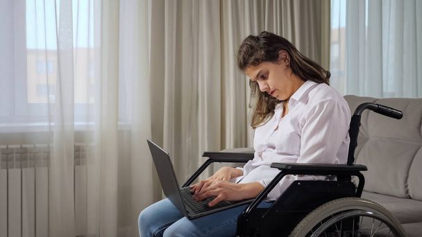 Gehandicapte vrouw werkt online op laptop zittend in rolstoel - Foto, afbeelding