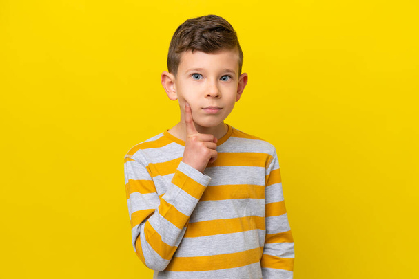 Kleine blanke jongen geïsoleerd op gele achtergrond en denken - Foto, afbeelding