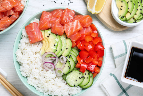 Delicious poke bowl with salmon and vegetables served on white wooden table, flat lay - Foto, afbeelding