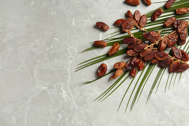 Tasty sweet dried dates and palm leaf on light table, flat lay. Space for text - Foto, immagini