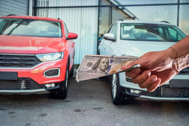 sterke mannelijke handen met nieuwe dollarbiljetten in de showroom van de auto. Het concept van het verkopen en kopen van een auto. Het concept van showrooms - Foto, afbeelding
