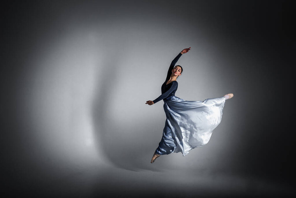 jovem bonita, frágil, bela bailarina dançando em um vestido azul longo em um fundo uniforme, chave baixa. Ballet, dança, dançarina - Foto, Imagem