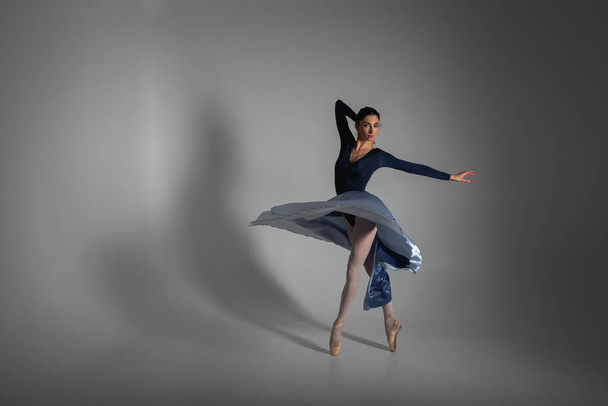 молодая красивая, хрупкая, красивая балерина, танцующая в длинном голубом платье на однородном фоне, сдержанная. Балет, танцы, танцоры - Фото, изображение