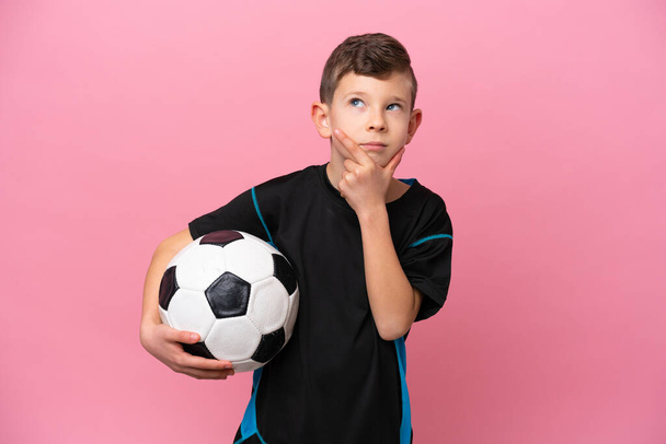 Kis kaukázusi focista fiú elszigetelt rózsaszín háttér, amelynek kétségei vannak - Fotó, kép