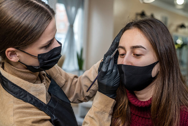 a beautiful young client in a special black mask came to the salon for makeup during a pandemic. The concept of beauty services during a pandemic - Photo, Image