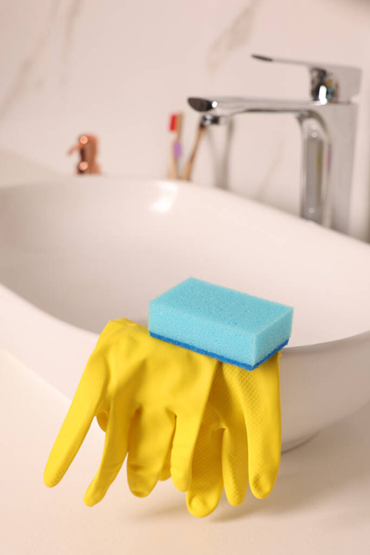 Sponge and rubber gloves on bathroom sink indoors - 写真・画像