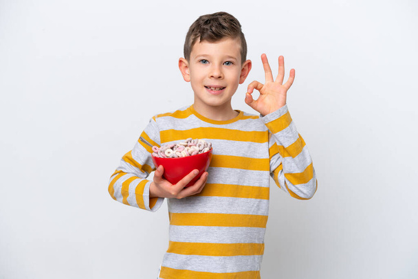 Kis kaukázusi fiú gazdaság gabona tál elszigetelt fehér háttér mutató ok jel ujjakkal - Fotó, kép