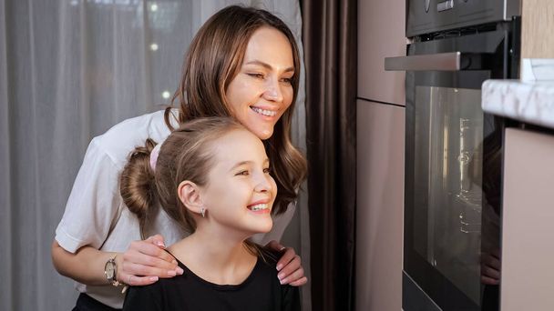 Mother explains teen daughter cooking food process in stove - Fotografie, Obrázek