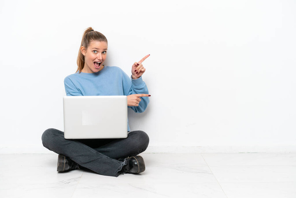 Młoda kobieta z laptopem siedząca na podłodze zaskoczona i skierowana bokiem - Zdjęcie, obraz