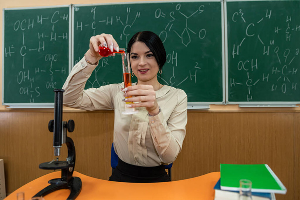 hermosa joven profesora de química con frascos en sus manos en el fondo del tablero con fórmulas escritas. Concepto de profesor de química - Foto, imagen