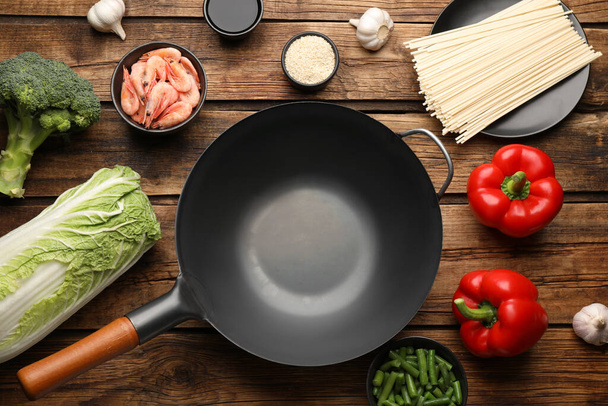 Empty iron wok and raw ingredients on wooden table, flat lay - Zdjęcie, obraz