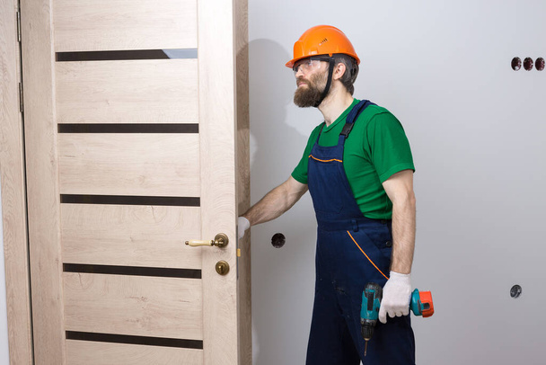 Un serrurier masculin installe une porte dans un appartement. Il travaille avec un tournevis.. - Photo, image