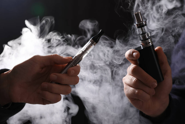 People with electronic cigarettes on black background, closeup - Фото, зображення