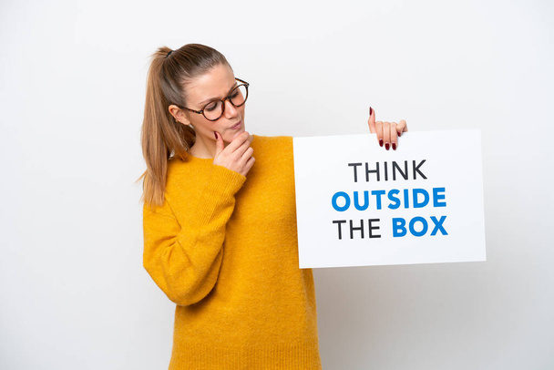 Jonge blanke vrouw geïsoleerd op witte achtergrond met een bordje met tekst Think Outside The Box en denken - Foto, afbeelding