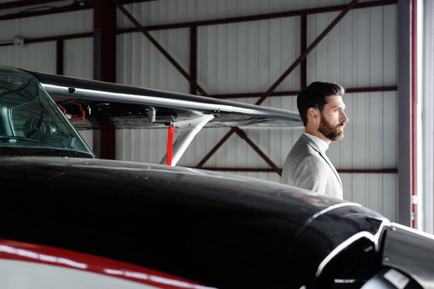 bearded businessman in suit looking away near helicopter on parking  - Foto, immagini