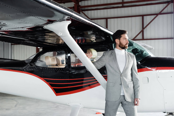 fiducioso uomo d'affari barbuto in giacca e cravatta in piedi vicino elicottero moderno - Foto, immagini