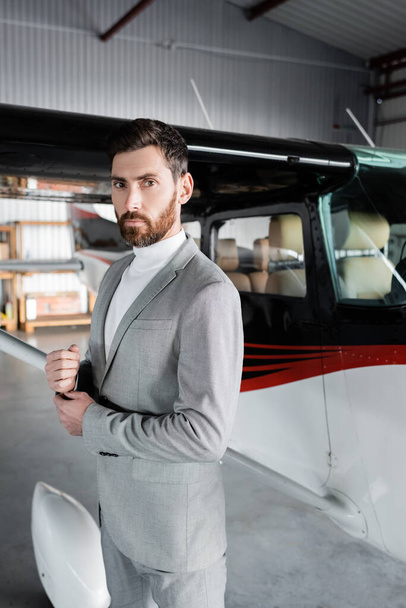 confident bearded businessman in suit looking at camera near modern helicopter - Valokuva, kuva