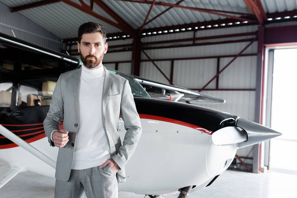 confident bearded businessman in suit standing with hand in pocket near modern helicopter - Foto, immagini