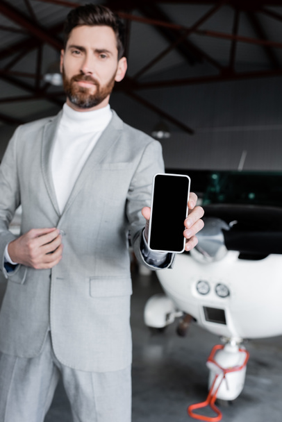 επιχειρηματίας σε επίσημη φθορά δείχνει smartphone με λευκή οθόνη κοντά στο σύγχρονο ελικόπτερο - Φωτογραφία, εικόνα