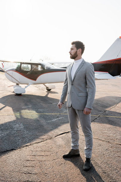 full length of serious businessman in suit standing near helicopter outdoors  - Valokuva, kuva