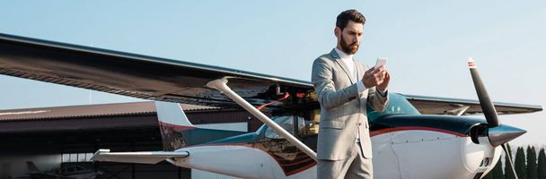 bearded businessman using smartphone near helicopter outdoors, banner - Foto, Imagen