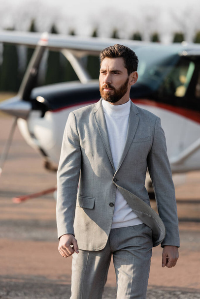 bearded businessman walking near blurred helicopter outdoors  - Foto, afbeelding
