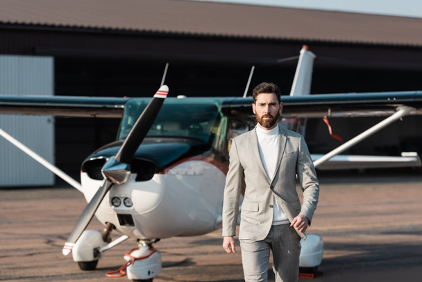 jóképű üzletember öltönyben sétál a modern helikopter közelében a szabadban  - Fotó, kép