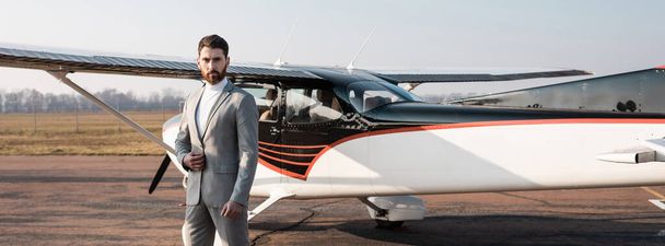 επιτυχημένος επιχειρηματίας στέκεται κοντά στο σύγχρονο ελικόπτερο και ρύθμιση σακάκι, πανό - Φωτογραφία, εικόνα