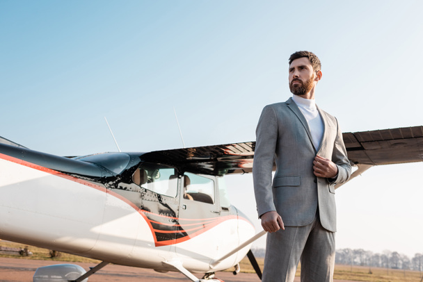 vista basso angolo di uomo d'affari di successo in giacca e cravatta in piedi vicino elicottero all'aperto  - Foto, immagini