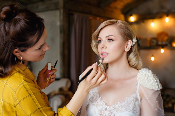 Make-up umělec maluje rty mladé blondýny s rtěnkou na její svatební den. Selektivní soustředění. Ráno nevěsty - Fotografie, Obrázek