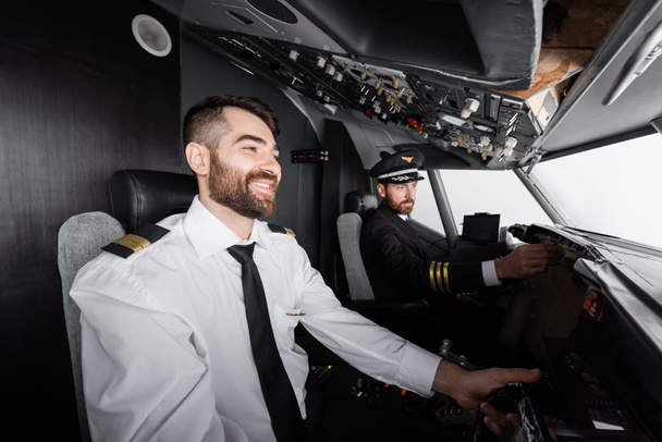 copilote joyeux en utilisant joug près du panneau de commande d'atteinte du commandant de bord dans le simulateur d'avion  - Photo, image