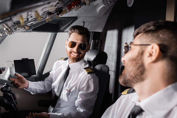 cheerful pilots in sunglasses looking at each other in airplane  - Foto, Imagen