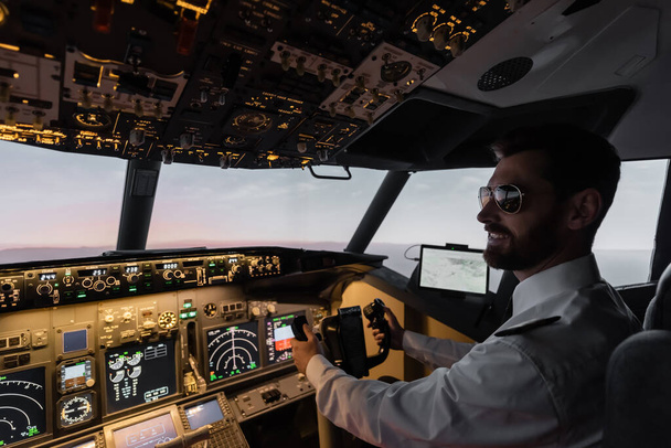 pilota allegro in occhiali da sole utilizzando giogo durante il pilotaggio in serata  - Foto, immagini