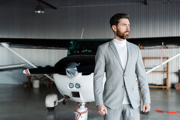 szakállas férfi szürke öltönyben áll a modern helikopter mellett  - Fotó, kép