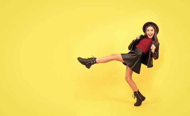 happy teen girl in hat and leather clothes making wide step forward, copy space, having fun - 写真・画像