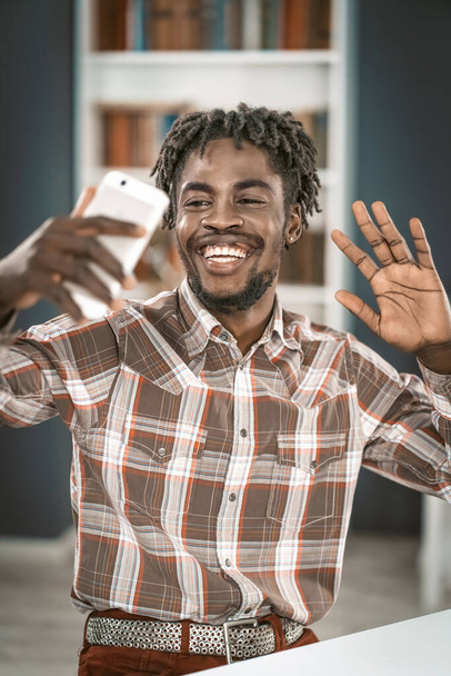 African American student having video call or taking selfie hold his phone in hand in front. Portrait of happy man gesturing looking at smartphone camera. Social media concept - Foto, Bild